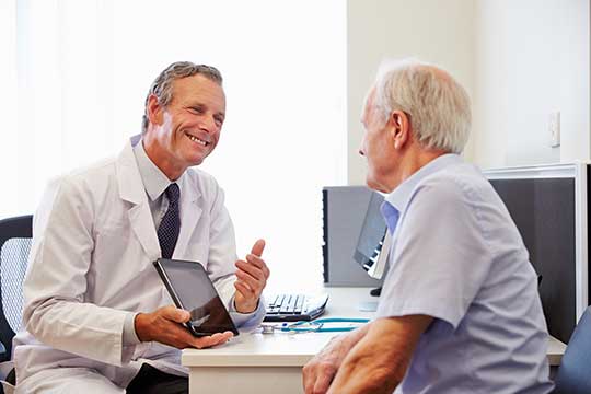 Audiologist showing a senior man hearing aid assessment details on a tablet